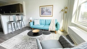 A modern living room with a sofa, two side tables, a coffee table, and a kitchen area with bar stools. - Sleepover | Pristine 1BD/1BA + Gym - Cincinnati (Cincinnati)