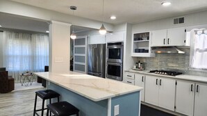 Een moderne keuken met witte kasten, een marmeren eiland, roestvrijstalen apparatuur en hanglampen.