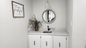Een badkamer met een wit wastafelmeubel, een wastafel, een spiegel en een geïnspireerd citaat in een lijst op de muur.