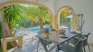 A dining area with a pool view, featuring a table with chairs, a hanging light fixture, and a stone bench. - La Terraza del Sol by Interhome (Jávea)