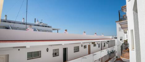 Ein mehrgeschossiges Wohngebäude mit Balkonen, einer flachen Dachterrasse und blauem Himmel.