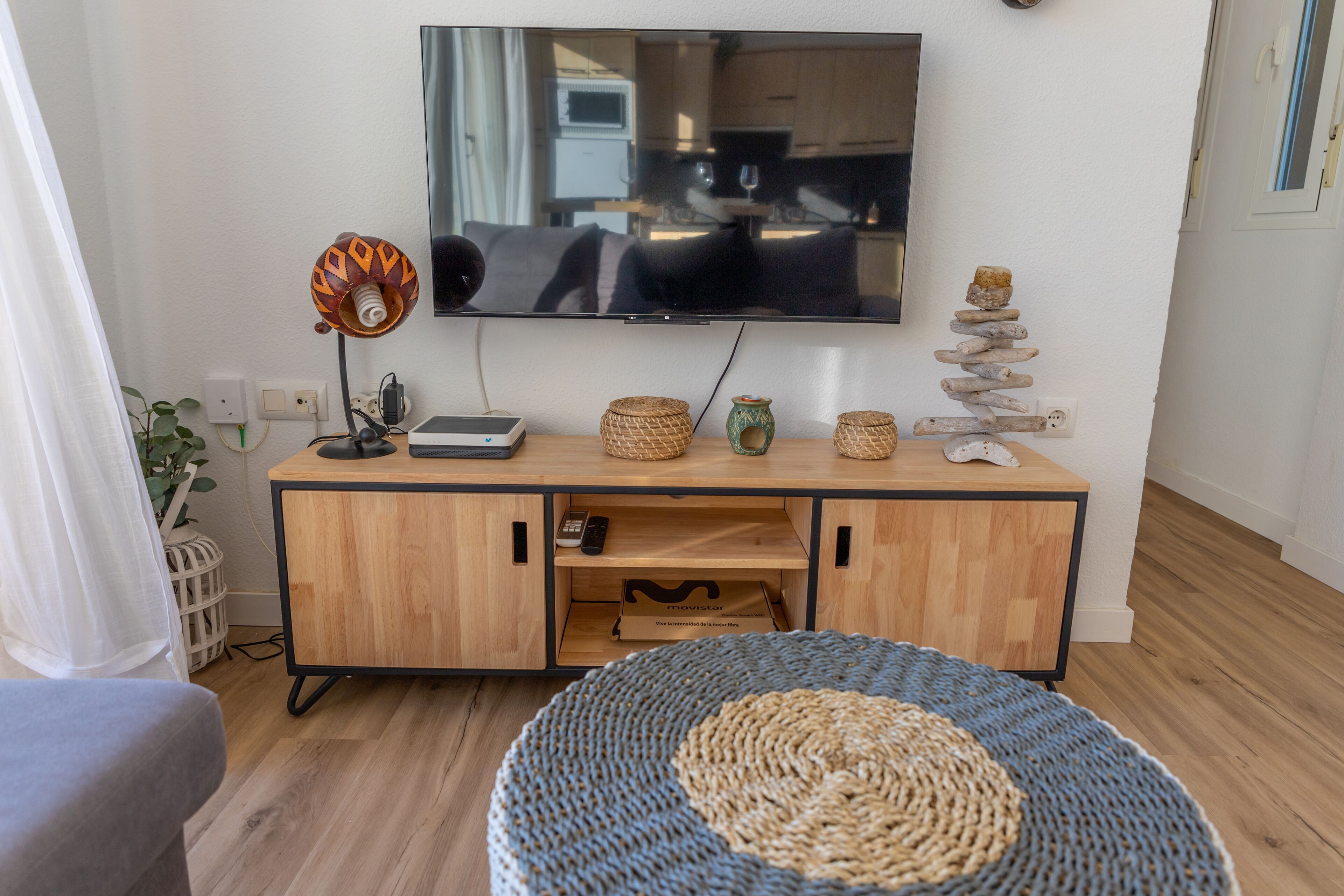 A living room with a wooden cabinet, a television, a lamp, and a woven rug.