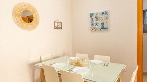 Et spiseområde med et glasbord, hvide stole og et spejl på væggen.