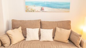 En beige sofa med fire puder, et maleri af en strandscene og en lampe til højre.
