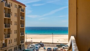 Vista da un balcone su una spiaggia, con un parcheggio e un edificio a più piani.