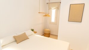 Una cama bien hecha con un cojín color beige, un tapete redondo pequeño, un perchero de madera colgante y un cuadro en la pared.