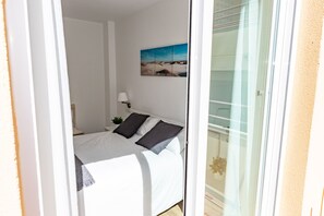 A bedroom with a bed, a nightstand, a lamp, and a painting on the wall. - Apartamento Sereno 3 | Piscina, Garaje, Terraza y Playa (Los Caños de Meca)