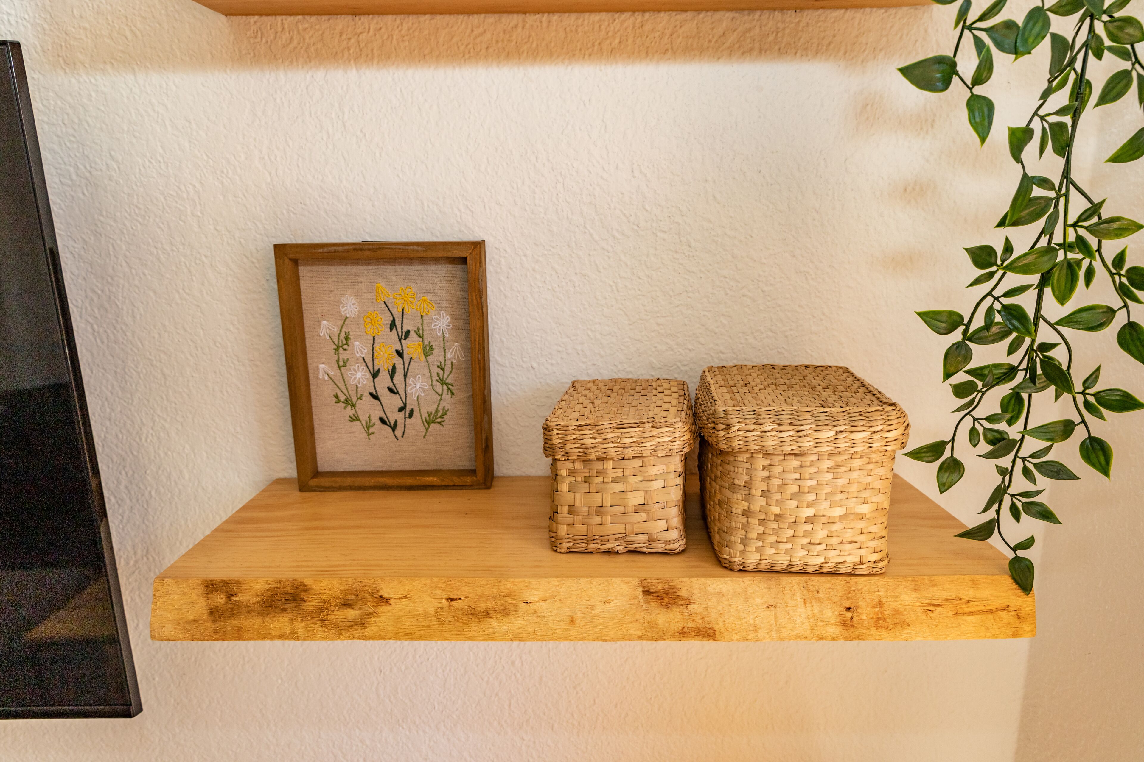 A wooden shelf with a framed floral artwork and two woven baskets.