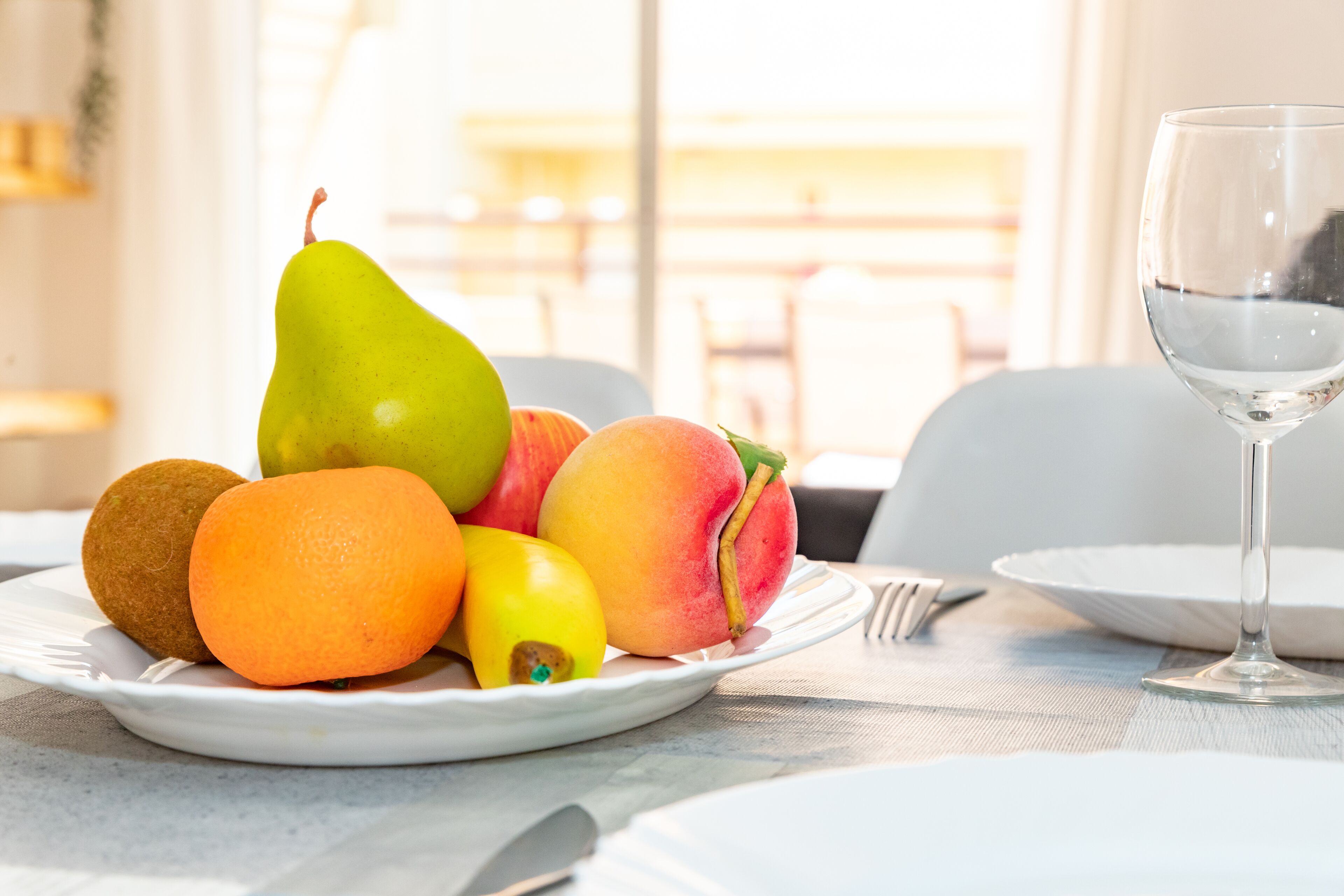 Ein Teller Obst mit Birne, Pfirsich, Orange und Kiwi, dazu ein Weinglas und Besteck auf einem Tisch.