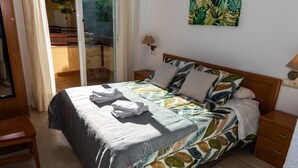 A neatly made bed with a patterned bedspread, a bedside table with a lamp, and a view of an outdoor balcony. - Apartamento Sereno 5 | Piscina, Garaje, Terraza y Playa (Los Caños de Meca)