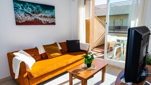 A living room with a sofa, a coffee table, a television, and a painting on the wall. - Apartamento Sereno 5 | Piscina, Garaje, Terraza y Playa (Los Caños de Meca)