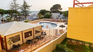 A rooftop pool area with a pool, lounge chairs, and a building with outdoor seating. - Apartamento Sereno 5 | Piscina, Garaje, Terraza y Playa (Los Caños de Meca)