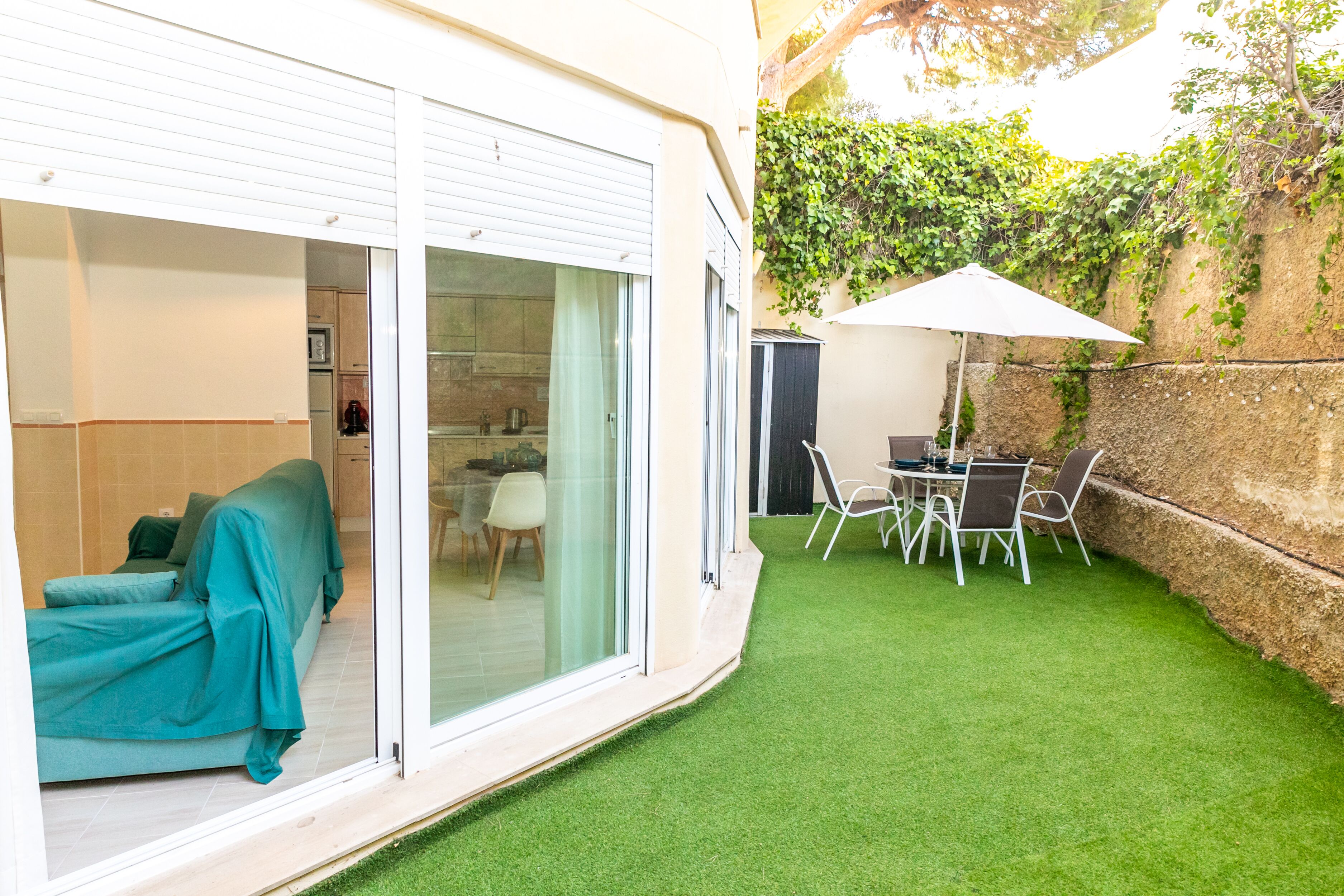 Une terrasse avec une table et des chaises, un canapé sous une pergola et une porte-fenêtre coulissante donnant sur la cuisine.