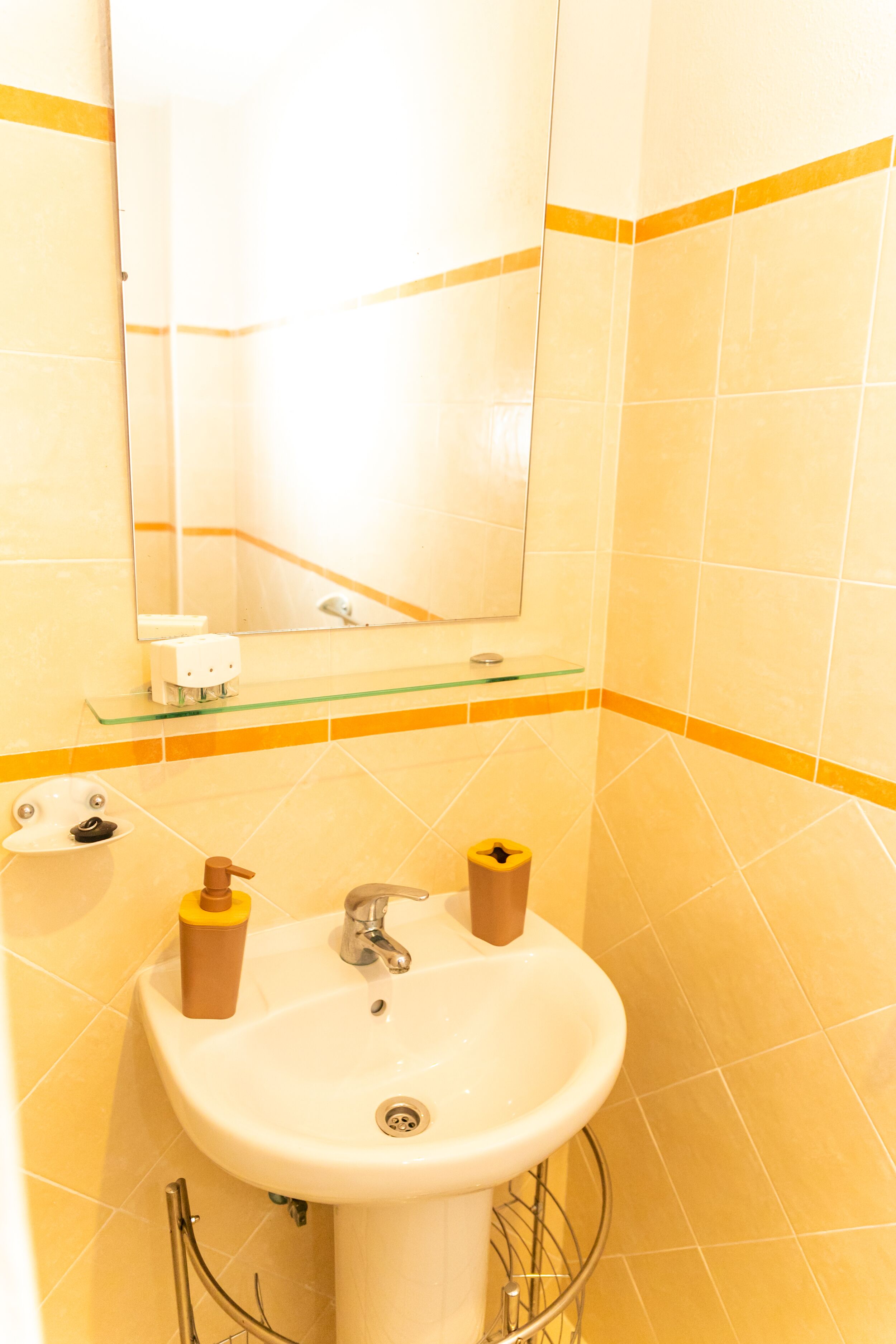 A bathroom with a white sink, a mirror, and yellow-tiled walls.