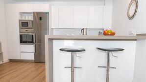 A modern kitchen with white cabinets, stainless steel appliances, and a wooden countertop with two bar stools. - Casa Los Hierros | Reformada Cerca Playa (Barbate)
