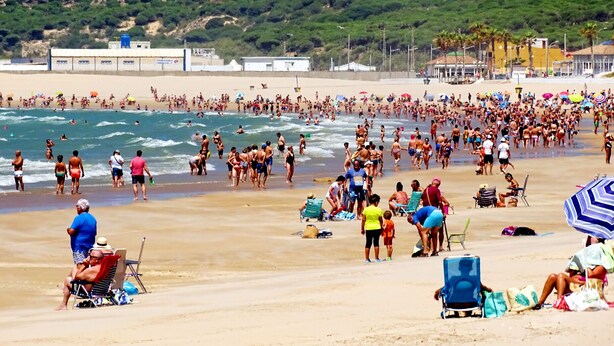 A crowded beach with people walking and swimming, and beach chairs and umbrellas. - Casa Los Hierros | Reformada Cerca Playa (Barbate)