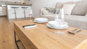 A modern kitchen with a wooden table set for dining, a sofa in the background, and a kitchen island with stools. - Casa Los Hierros | Reformada Cerca Playa (Barbate)