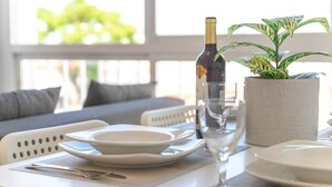 Een eettafel gedekt met borden, bestek, een fles wijn en een glas, met een plant en een raam op de achtergrond.
