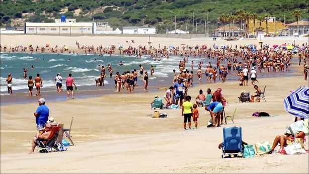Een druk strand met mensen die wandelen en zwemmen.