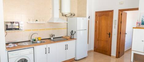 A compact kitchen with a washing machine, a microwave, and a refrigerator.