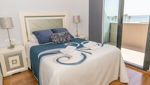 Habitación de hotel con cama, dos mesitas de noche, vistas a la playa y un balcón.