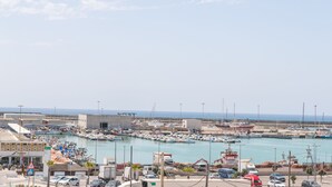 Un puerto deportivo con barcos, una carretera con automóviles y edificios al fondo.
