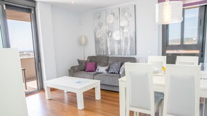 Una sala de estar moderna con un sofá gris, una mesa de centro blanca y un comedor con sillas y una mesa blancos.