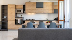 Une cuisine moderne avec des meubles en bois, un four à micro-ondes encastré et une cuisinière à gaz. On y trouve un coin repas avec une table et des chaises, ainsi qu’un canapé au premier plan.