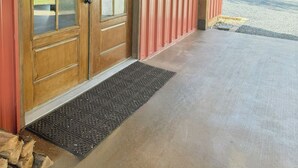 A wooden door with glass panels, a red exterior wall, and a concrete porch with a metal doormat.