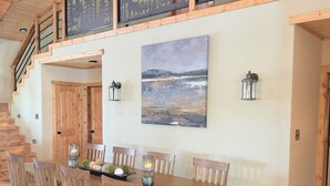 A dining area with a wooden table and chairs, a painting of a landscape, and a staircase with wooden railings.