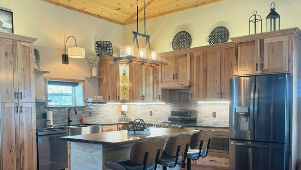 A spacious kitchen with wooden cabinets, a stainless steel refrigerator, and a central island with bar stools.