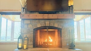 A stone fireplace with a flat-screen TV mounted above it, a fire burning inside, and two lanterns on the mantel.