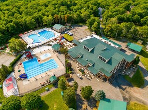 Eine Luftaufnahme eines Resorts mit einem großen Schwimmbecken, einem separaten Poolbereich und einem Gebäude mit grüner Dachbegrünung.