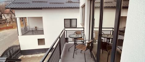 En balkong med ett bord och några stolar, ett litet fönster och utsikt över gatan.