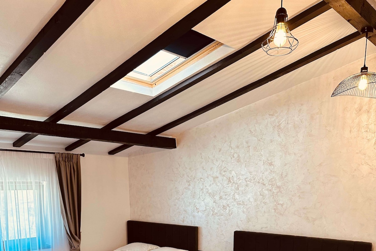 Habitación de hotel con dos camas, suelo de madera, tragaluz y pared con textura.