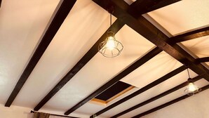 A room with exposed wooden beams, a hanging light fixture, and a window with curtains. - Casa Yda (Horezu)