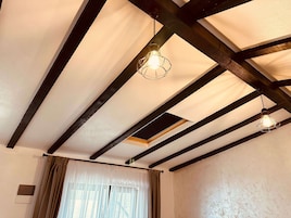 Una habitación con vigas de madera a la vista, un colgador de techo y una ventana con cortinas.