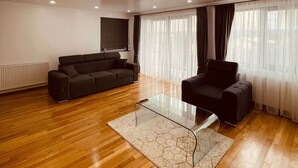 A modern living room with a wooden floor, a black sofa, a glass coffee table, and a ceiling light fixture. - Casa Yda (Horezu)