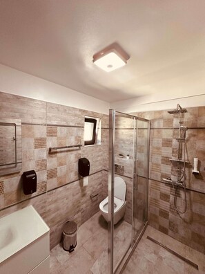 Un baño moderno con ducha acristalada, inodoro y secamanos.