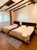 Habitación de hotel con dos camas, suelo de madera, un ventanal con cortinas y techo con vigas a la vista.