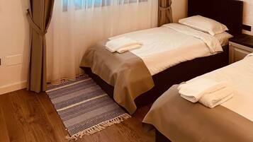 Een slaapkamer met een bed, nachtkastje, raam met dunne gordijnen en een kamerkleed met patroon.