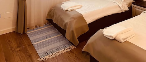 A bedroom with a bed, a bedside table, a window with sheer curtains, and a patterned rug.