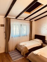Un dormitorio con cama, mesita de noche, ventana con cortinas translúcidas y una alfombra estampada.