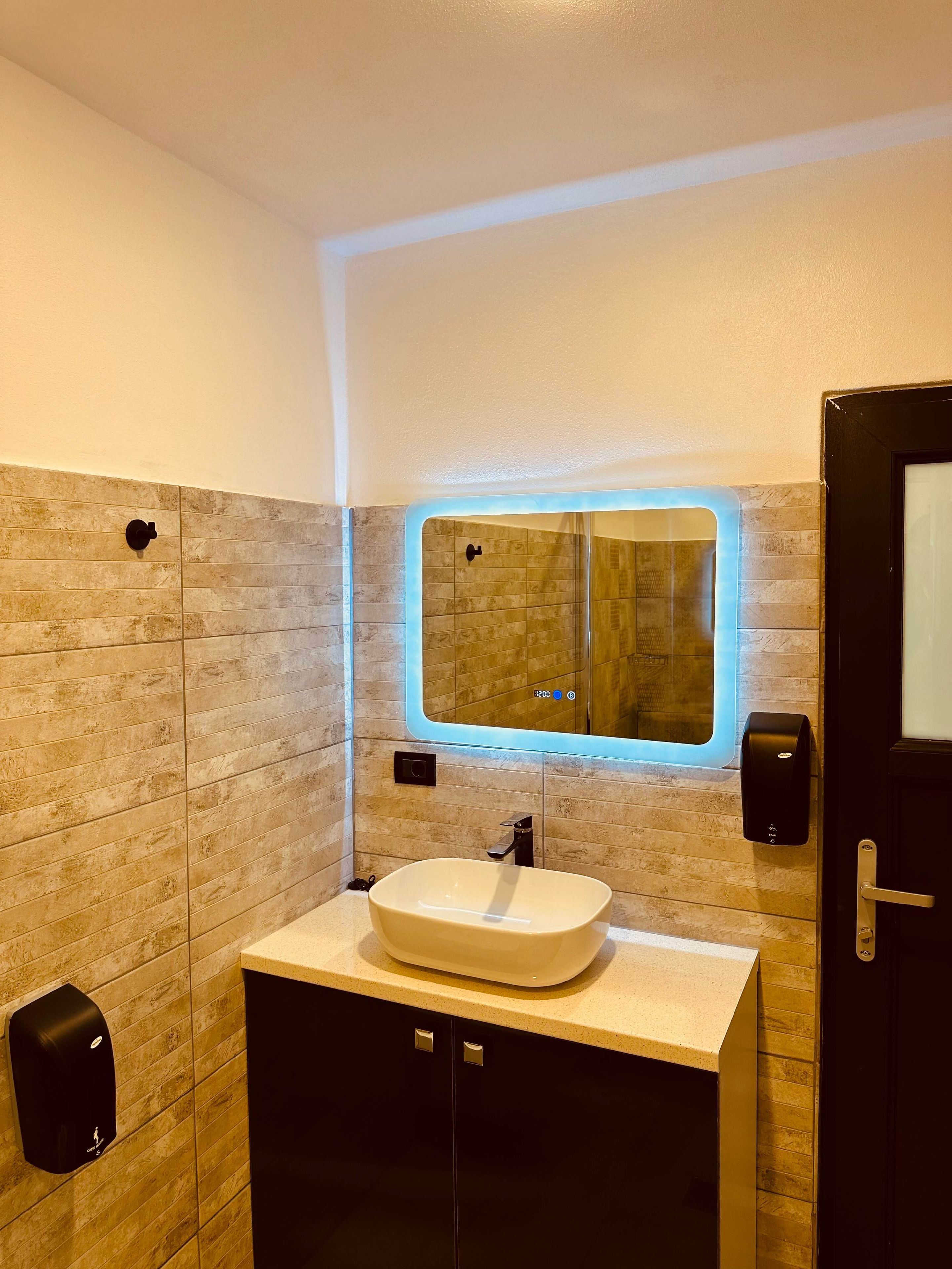 Een moderne badkamer met een grote spiegel, een wastafel en een handdesinfecterend middel.