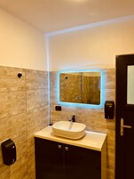 Un baño moderno con un espejo grande, un lavabo y un dispensador de gel antibacterial.