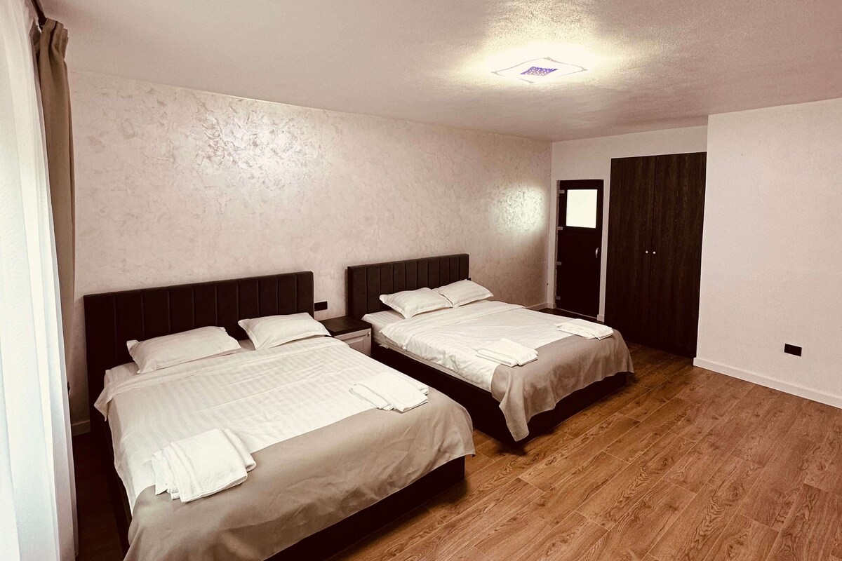 Una habitación de hotel con dos camas, suelo de madera y una puerta que da a otra habitación.
