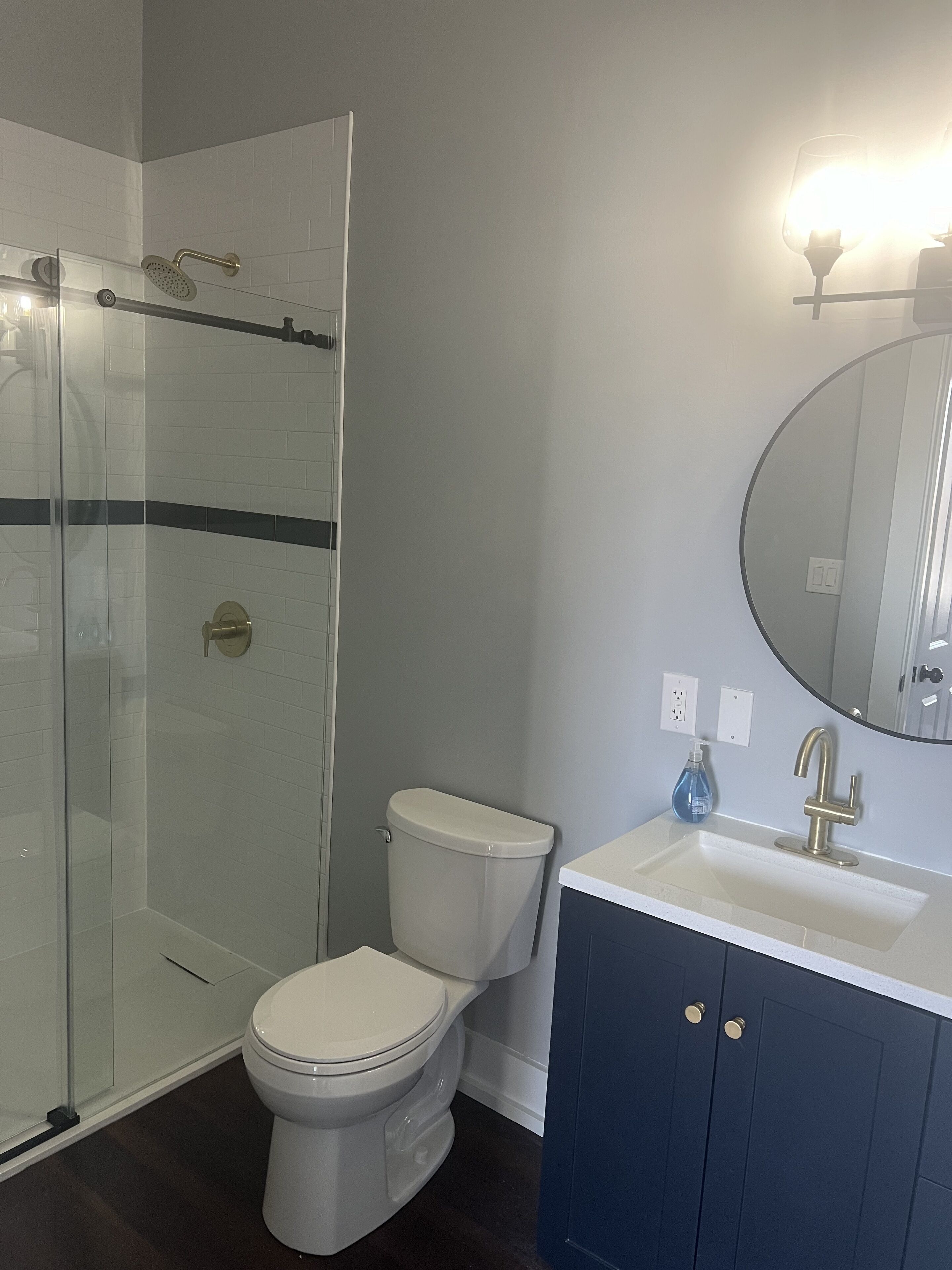 Une salle de bain avec une douche à parois de verre, des toilettes blanches, un lavabo avec un miroir et des meubles bleus.