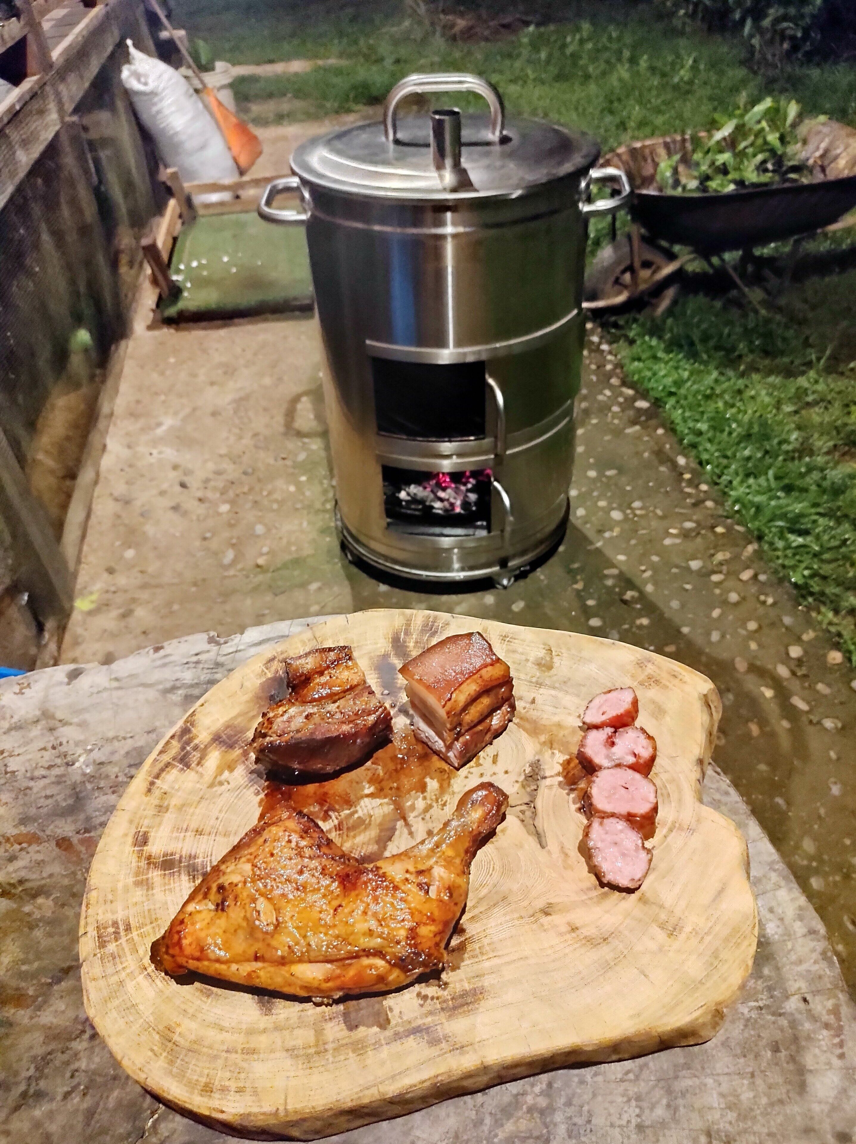 A portable cooking stove with a pot on a concrete surface, surrounded by a garden area.