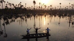 A calm water body with tall palm trees in the background and a small boat with three people. - Quirquincho House (Tambopata)