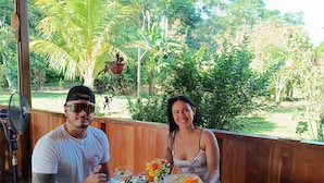 A wooden table with a rustic design, surrounded by a wooden fence, with a view of lush greenery and trees in the background. - Quirquincho House (Tambopata)
